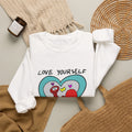 White Love Yourself Schnerd Crewneck Sweatshirt, styled on a table with the character print visible